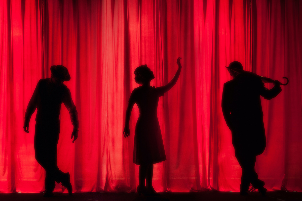 Theatre performance with actors in shadow in front of a bright red curtain