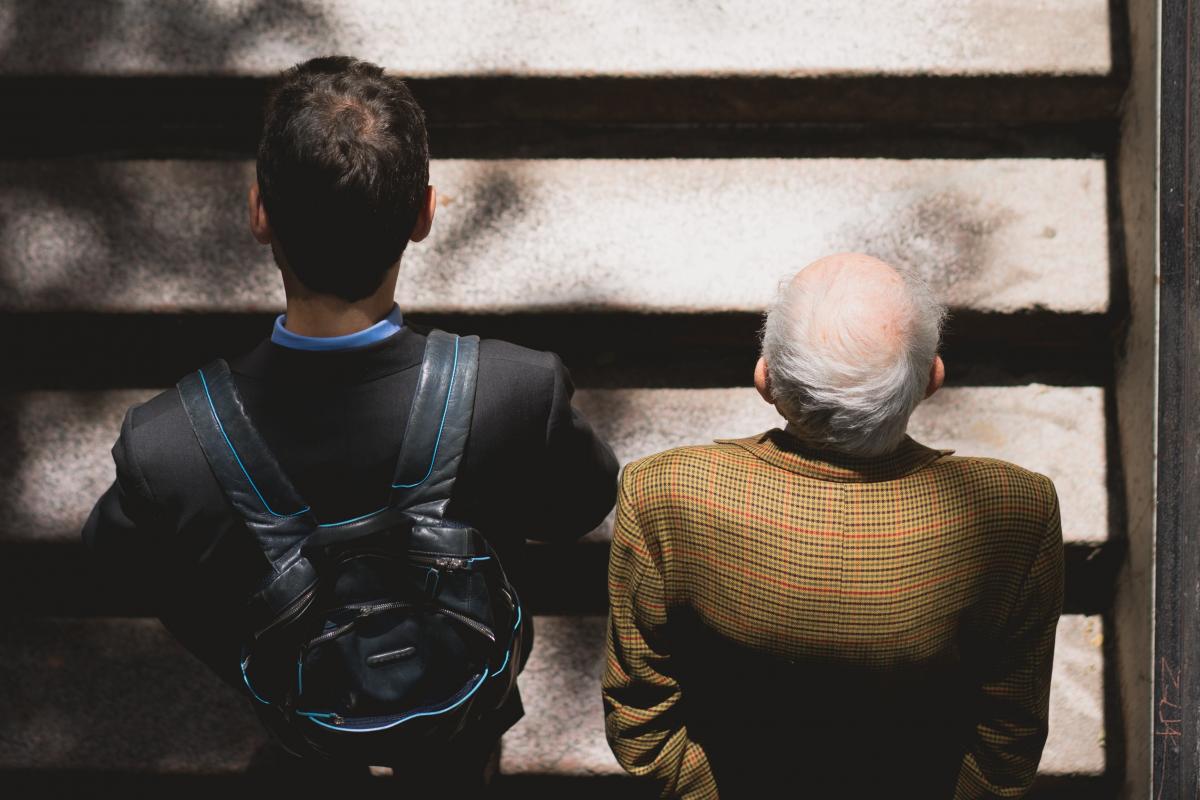 A younger man walks up a set of stairs listening to an elderly man.