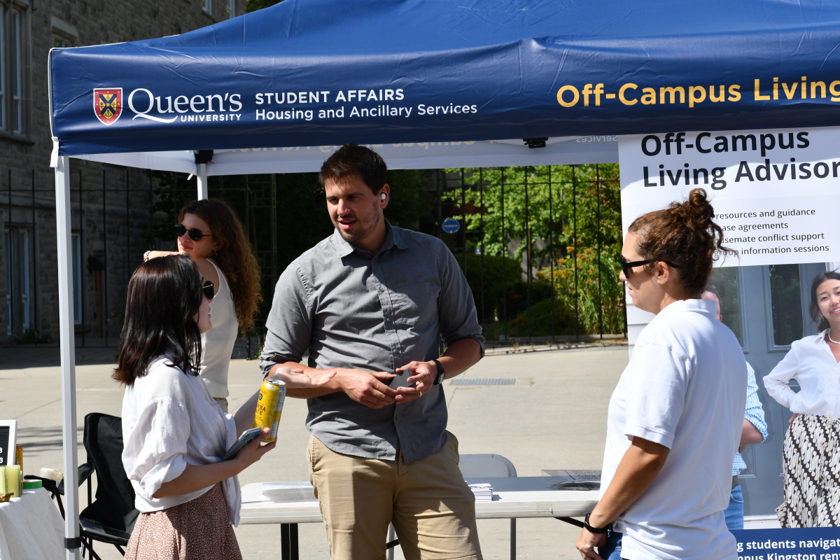 Photograph of Queen's Off-Campus Living Advisor speaking with students at the ASUS Sidewalk Sale.