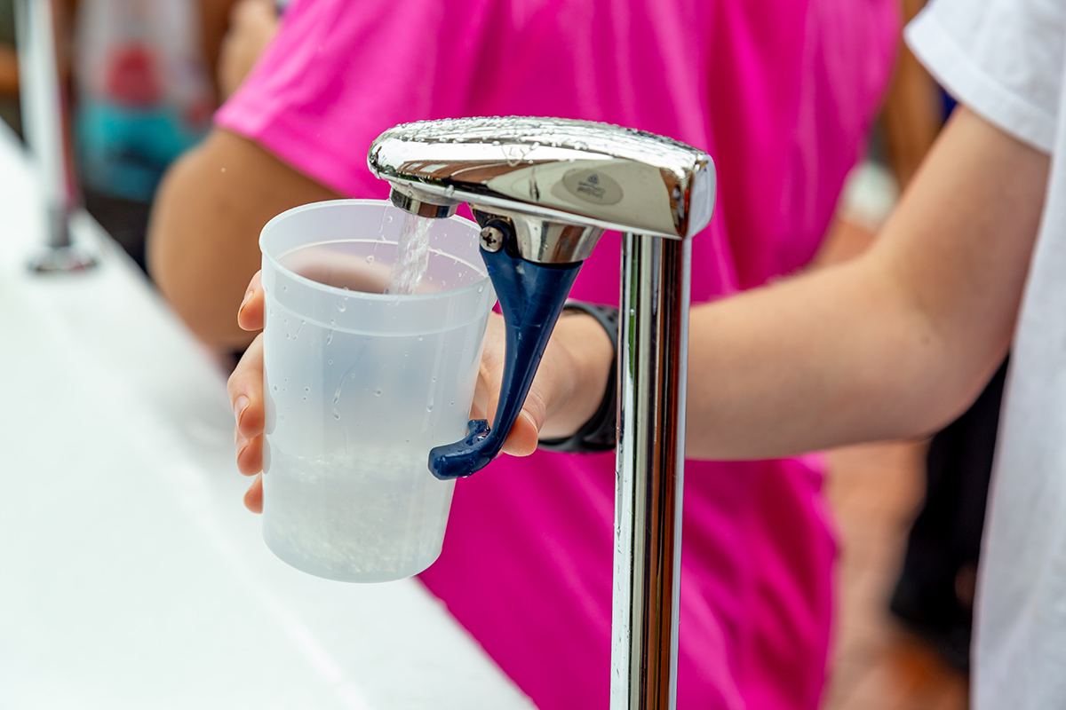 Children fill a plastic cup with water from a tap.