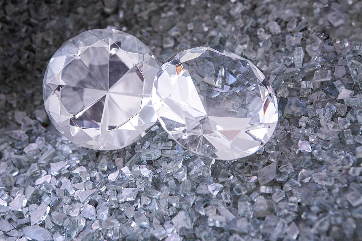 Two cut diamonds displayed on grey sand.