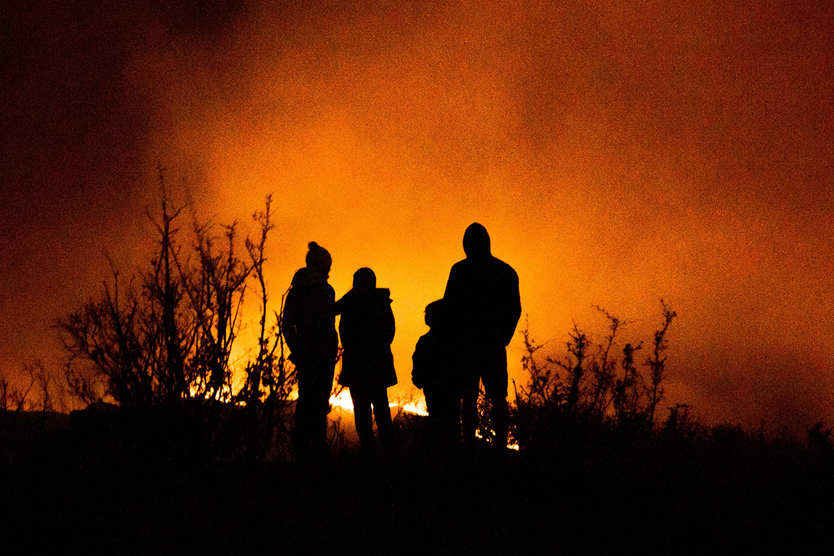 A family watches a wildfire from the safety of a ridge.