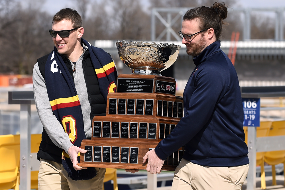 Photograph of Queen's Football alumni from 2009 Vanier Cup winning team carrying the cup at announcement event.
