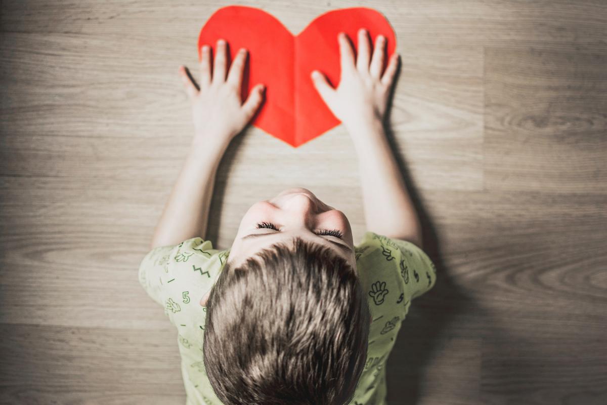 Child holding red paper shaped as a heart (Photo by Anna Kolosyuk, Unsplash)