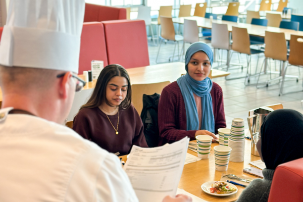 Photograph of Hospitality Services chef offering students from Queen's University Muslim Student Association a tasting of the dining hall's Ramadan menu.