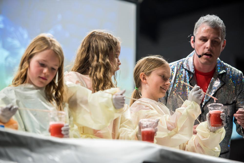 Photograph of Charlie Hindmarch (Medicine) performing a strawberry DNA extraction demonstration on stage.