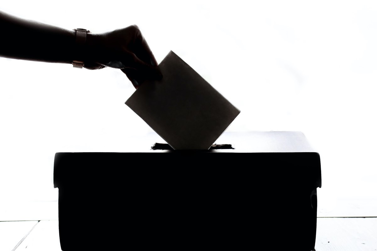 A person, in silhouette, puts a ballot in a ballot box.