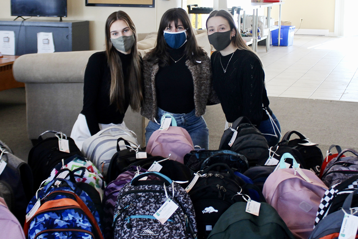 Bags of Promise team members pose behind a selection of backpacks