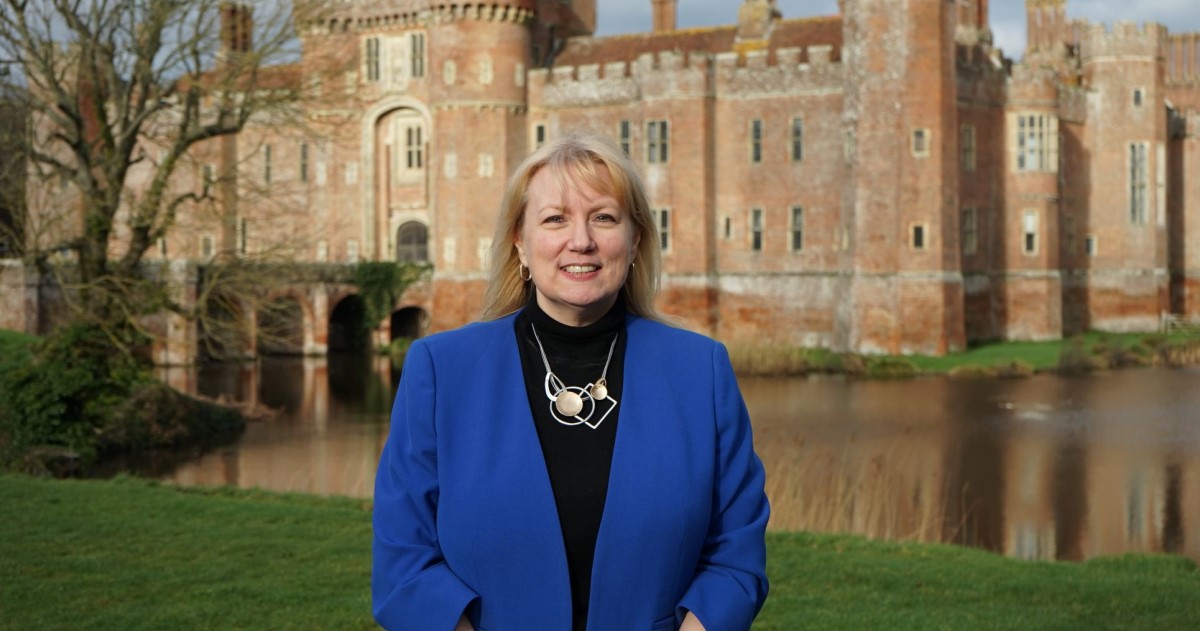 [Janine Griffiths-Baker in front of Herstmonceux Castle wearing a blue blazer]