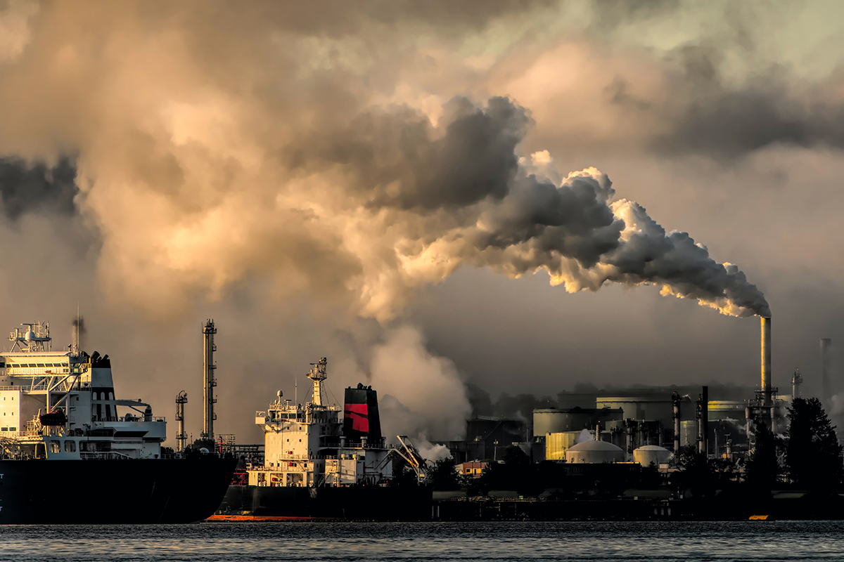 Tankers ships wait at a refueling station where a smokestack releases smoke.