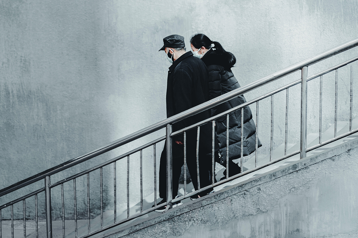 A couple wearing masks descend concrete stairs.