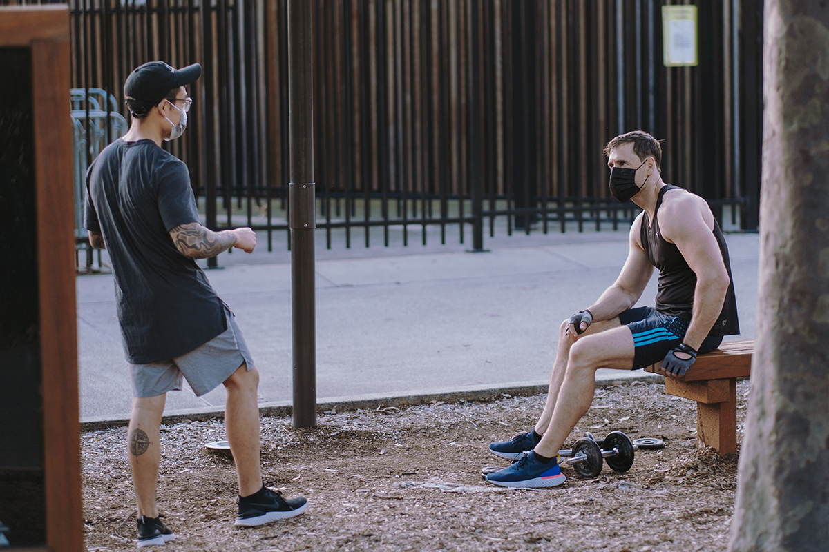 Two men wearing masks speak with each other during an outdoor workout. 