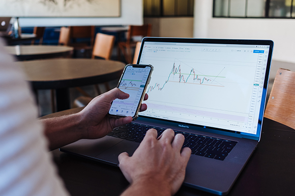 A man floolws the stock market with a phone and computer.
