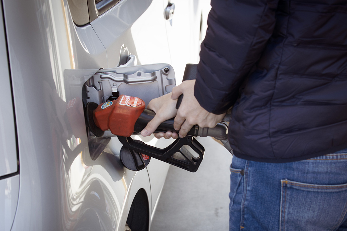 A man pumps gasoline into a silver car