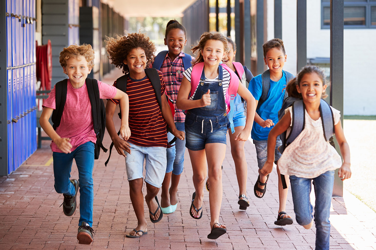 A group of school-age children run outside a school.