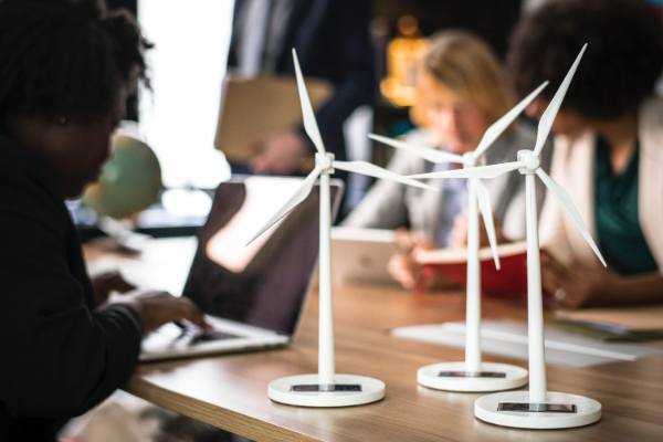 Small windmill models on a table next to people working on laptops.