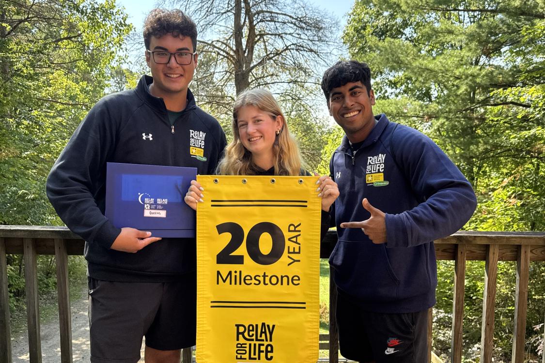 Three students holding a yellow 20 year Relay for Life banner 