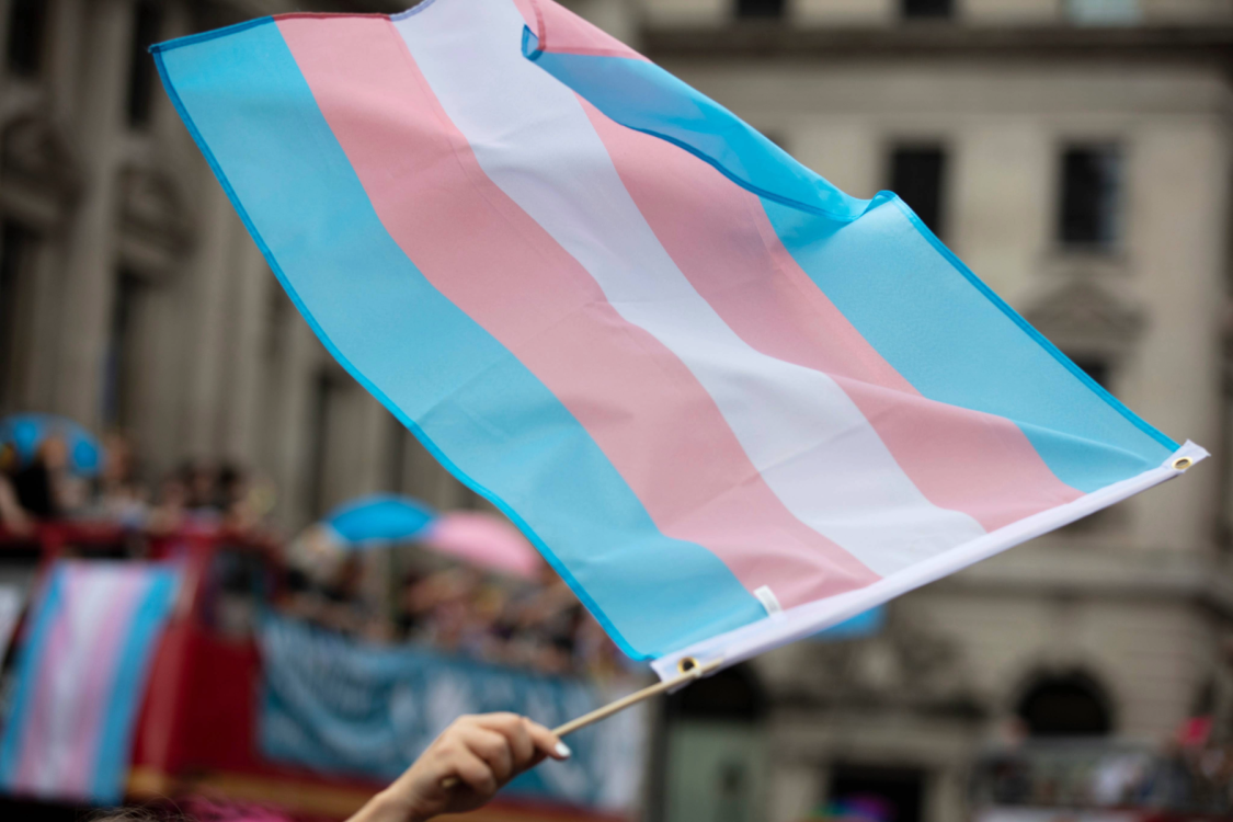 A trans pride flag being waved in the air