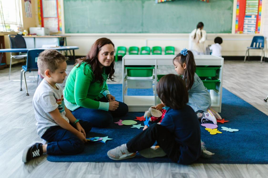 Teacher sitting with kindergarten students on carpet in classroom.
