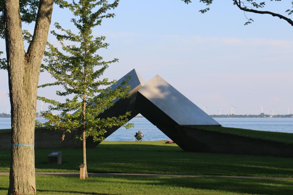 View of park by lakefront with two metal beams coming out of ground (sculpture).