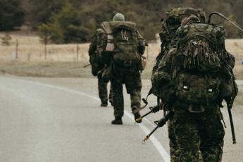 Canadian soldiers with backpacks march along a country road.