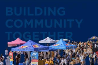 Photograph of ASUS Sidewalk Sale with the words "Building Community Together" in the background.