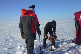 [Using an ice auger to drill a hole through the ice on Great Slave Lake, March 2014. The red tent is set up to provide shelter and to heat water for thawing equipment.  Credit: Marlene Evans, Environment and Climate Change Canada (ECCC)]