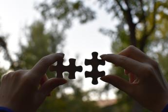 Two hands holding two puzzle pieces together.