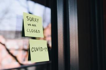 A Post-It note on glass door announces a business is closed due to COVID-19.