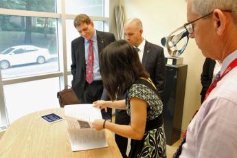 [Clarrie Lam Manager, Facilities and Operations at Q-CPU shows Principal Daniel Woolf and Provost Benoit-Antoine Bacon the floor plan and architectural renderings of the facility.]