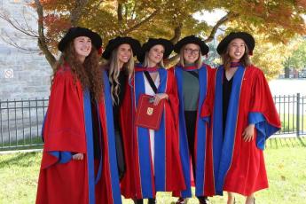 students in grad robes posing under a tree