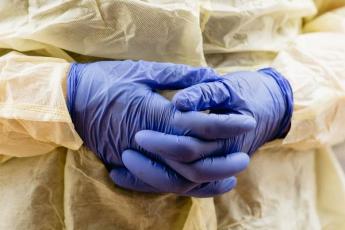A nurse wearing blue protective gloves folds their hands in front of them.