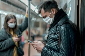 A young man wearing a mask on a subway looks at his cellphone
