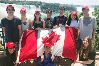 "Australian students participating in Queen’s Political Studies Summer Institute hold a Canadian flag as they stand in front of Niagara Falls"