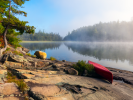 A canoe pulled up on a rocky beach at a lake.