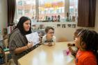 A teacher instructs three children at a table.