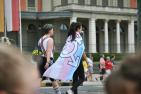 Two women, one wearing a transgender flag, walk on a city street.