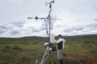 Man standing in a marsh installing a tower shaped research device 