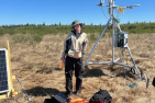Young woman wearing a bucket hat standing in a wetland with a research tower 
