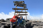 two people posing in front of the sign at the top of the mountain 