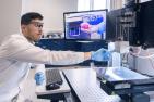 Student at 3D printer with 3D printed heart on monitor in background