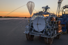 Radio telescope and balloon against an orange sky 