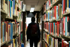 A silhouette of a student walking between library book stacks