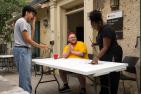 Three people standing over a table with paintbrushes, in front of house.