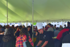 Man wearing chef's hat serving food inside large event tent.