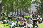 Many people sitting on lawn eating food during sunny day.