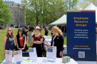 Four smiling women standing behind table with a banner reading "Employee Resource Groups"