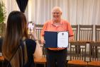 Woman taking a photo of a man wearing coral button up holding open a formal binder.