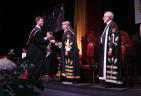Young man walking across stage at convocation shaking hand with Shelagh Rogers.