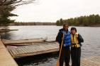 Two people holding canoe paddles standing by pier with life jackets on.